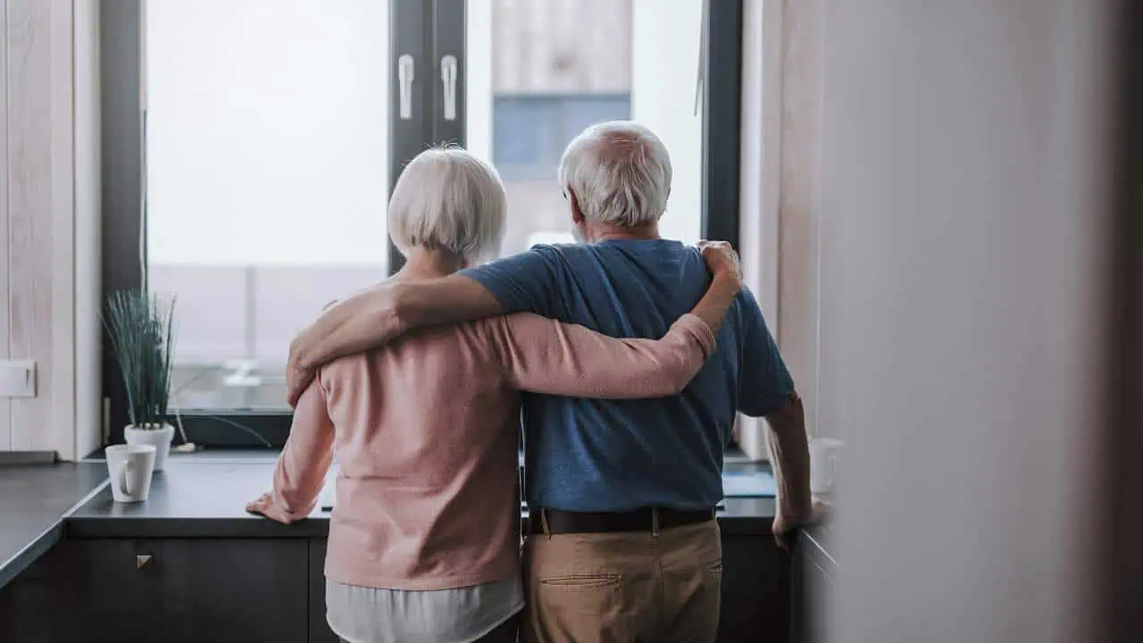 old couple standing at home looking at solar panels out of window